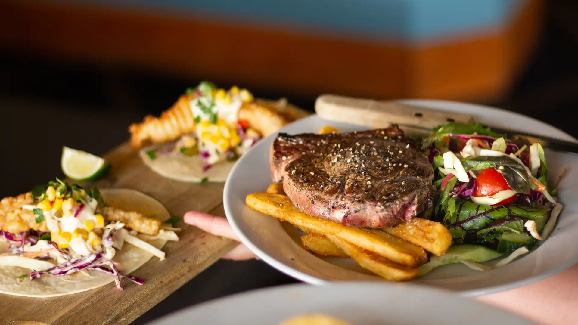 Ein Teller der mit Steak und Pommes anrichtet an den Tisch gereicht wird